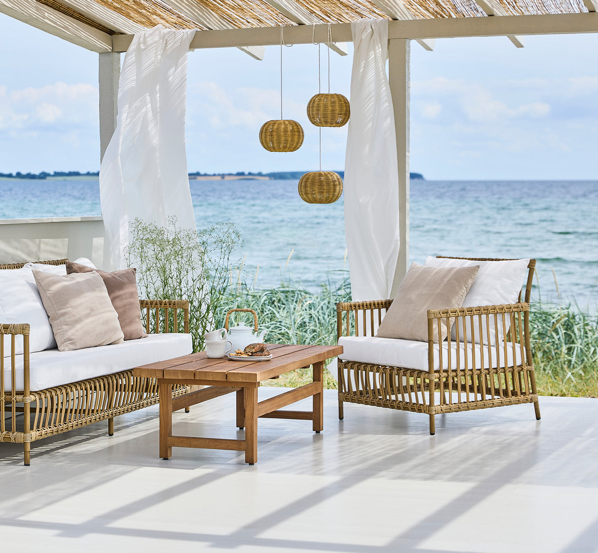 Esta es una imagen de estilo de vida de Caroline sillón lounge exterior en antique Aluminium ArtFibre, en una terraza de madera junto al agua con.