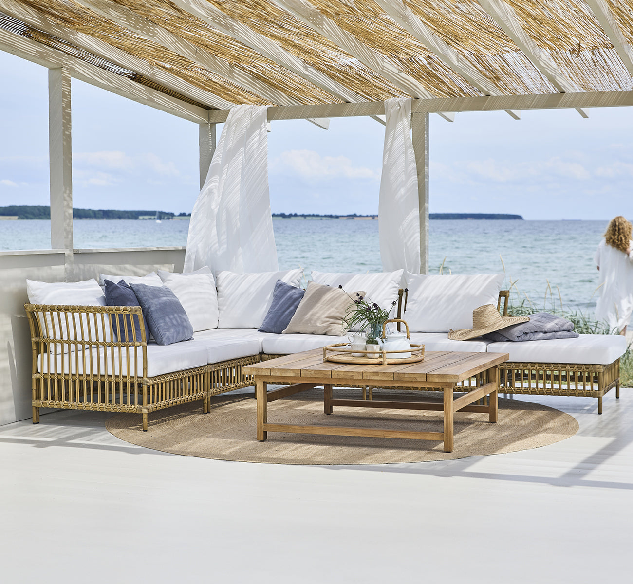 Esta es una imagen de estilo de vida de Maggie Sofá Módulo Central en antique aluminium artfibre. Pabellón de playa con sofá modular y vista al mar.
