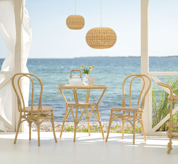 Esta es una imagen de estilo de vida de Tony mesa de café exterior en natural aluminium artfibre. En una terraza junto al mar con sillas, lámpara colgante y vista al océano.