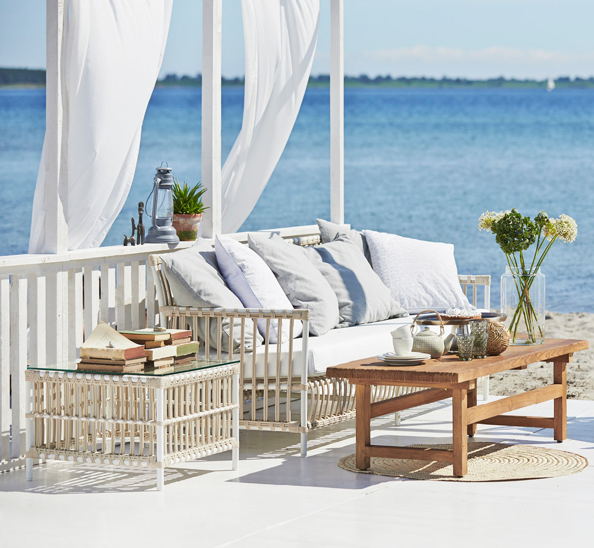 Esta es una imagen de estilo de vida de Caroline mesa exterior en dove White Aluminium ArtFibre, en una terraza de madera junto al agua con.