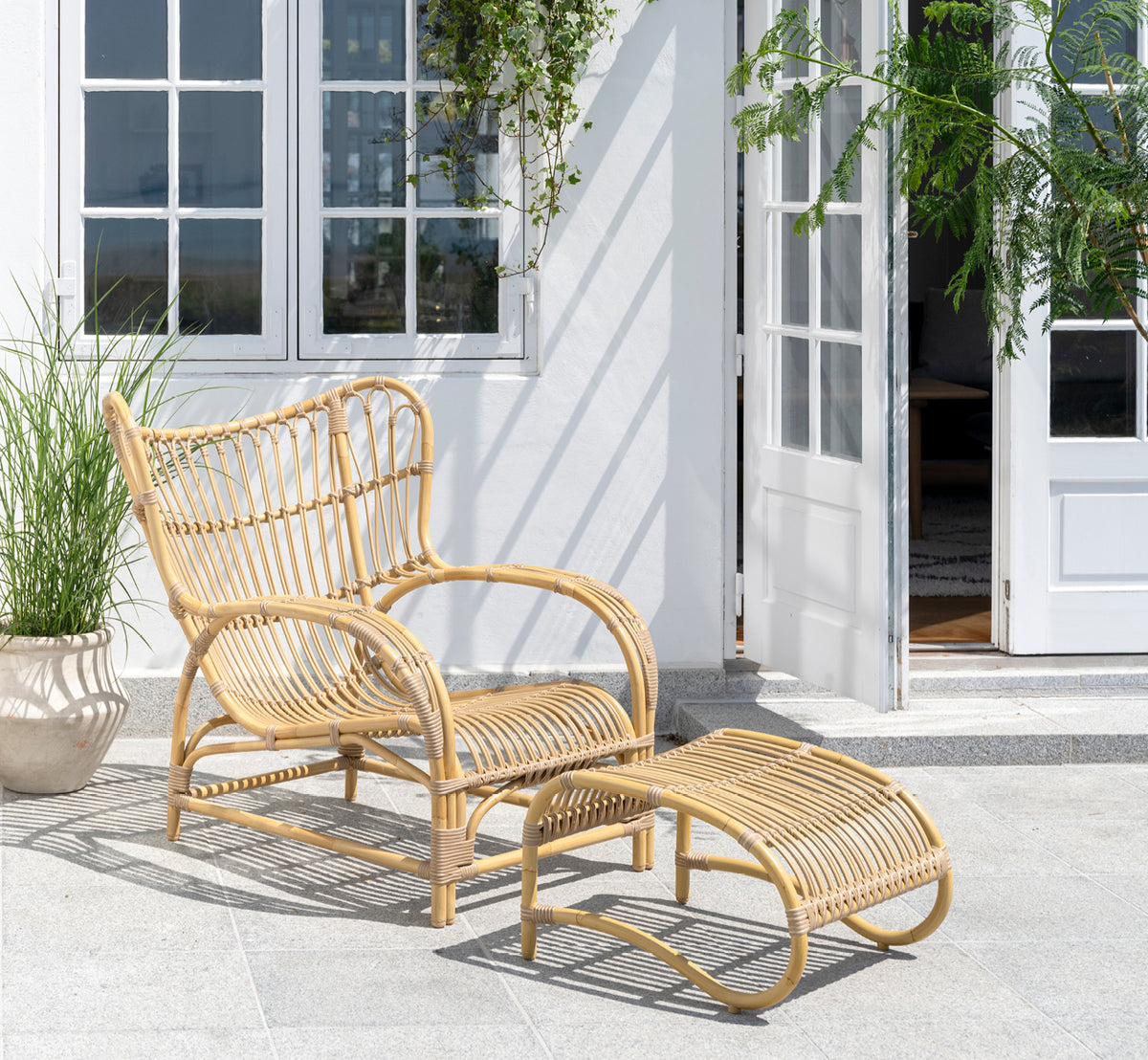 Esta es una imagen de estilo de vida de Teddy reposapiés exterior en natural aluminium artfibre. Combinado con el sillón lounge a juego en una terraza pavimentada soleada.