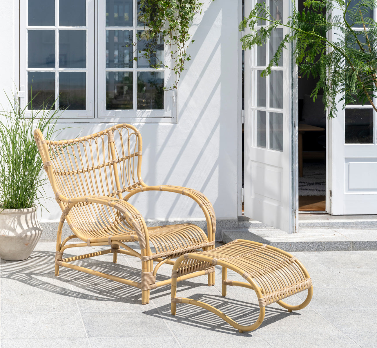 Esta es una imagen de estilo de vida de Teddy reposapiés exterior en natural aluminium artfibre. Combinado con el sillón lounge a juego en una terraza pavimentada soleada.
