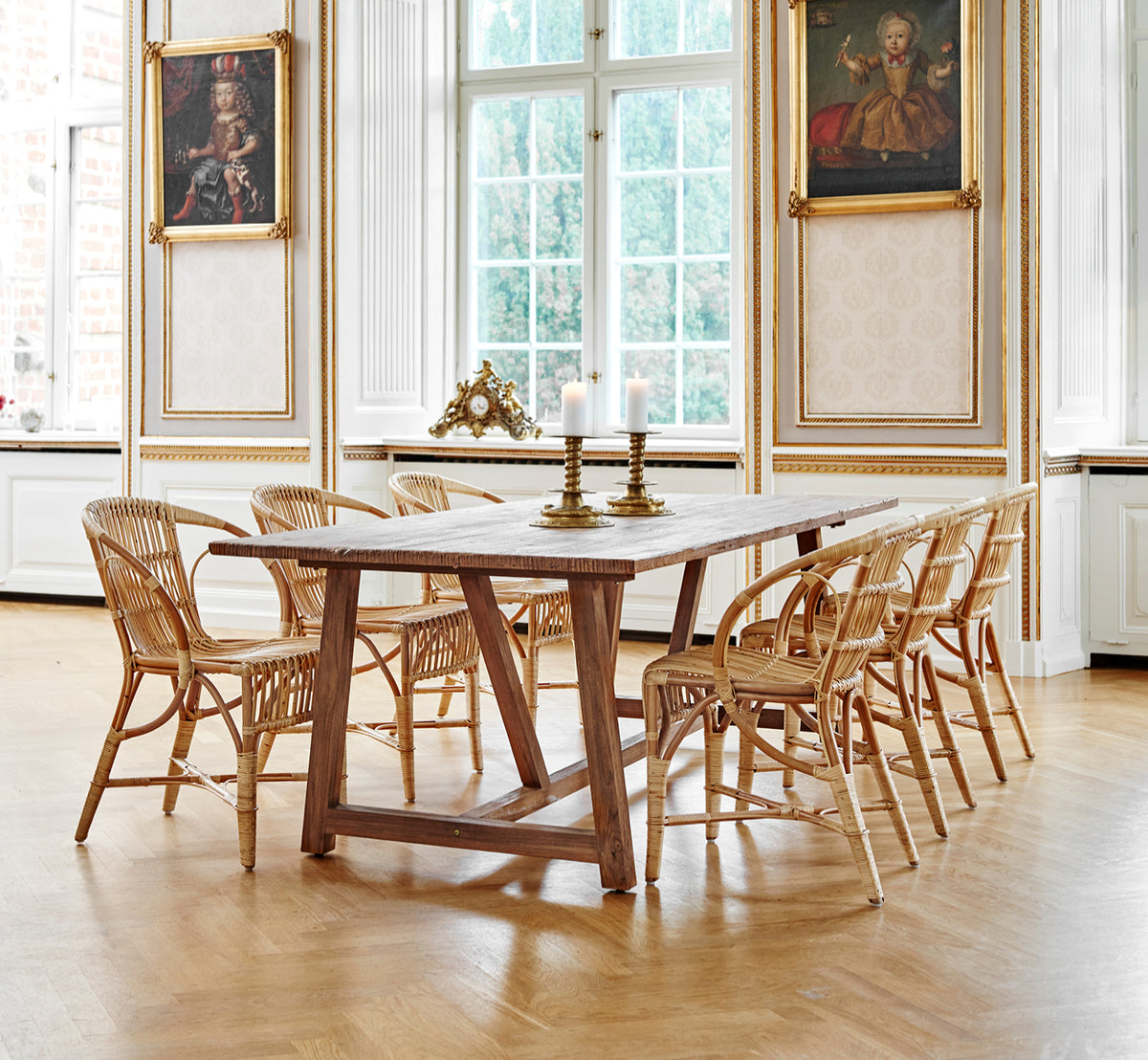Esta es una imagen de estilo de vida de Robert silla de comedor en polished antique rattan. Colocada junto a una alta urna de terracota sobre un suelo de parqué en espiga.