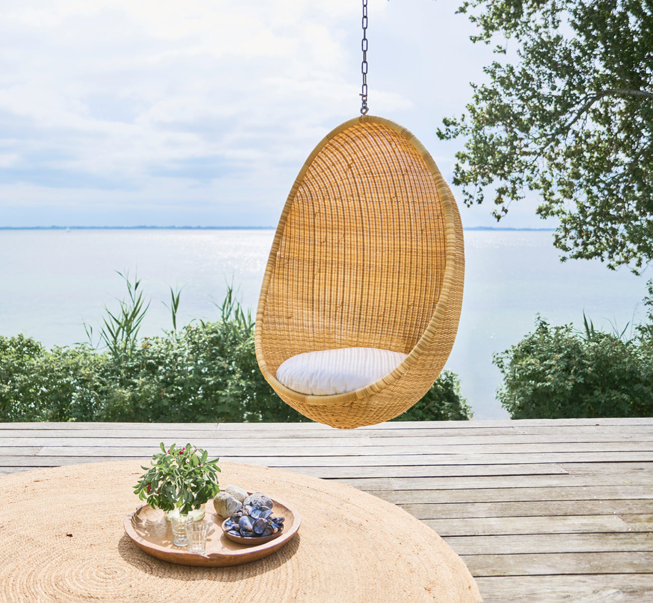 Esta es una imagen de estilo de vida de Hanging silla colgante exterior en natural core weave ArtFibre Aluminium, colgado de una pérgola blanca con.
