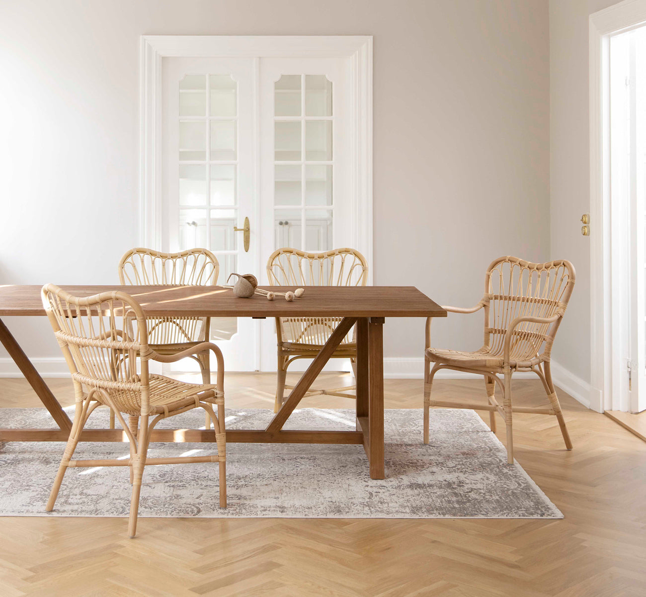 Esta es una imagen de estilo de vida de Lucas Teak Dining Table 240X100 cm en teak indoor. Con sillas de ratán en una habitación luminosa con suelo de roble en espiga.