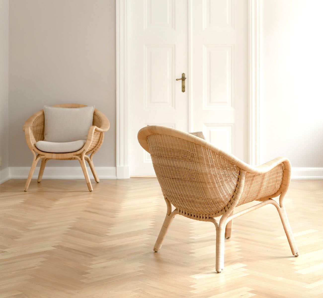 Esta es una imagen de estilo de vida de Madame sillón lounge en natural core weave rattan frame. Sala luminosa con suelo en espiga y puertas dobles blancas.