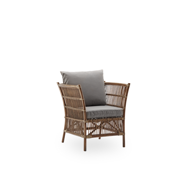 Vista lateral del sillón lounge de mimbre Donatello en color marrón antiguo. El sillón lounge tiene un diseño cuadrado con líneas estrictas, hecho a mano con ratán indonesio de alta calidad.