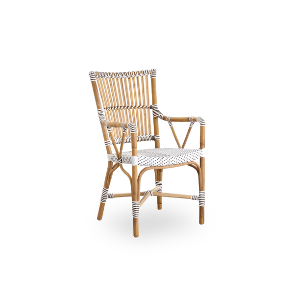 Vista lateral de la silla de comedor con brazos Monique. Estructura de ratán con asiento tejido en ArtFibre blanco con puntos marrones. Inspirada en el diseño de bistró de los años 50.