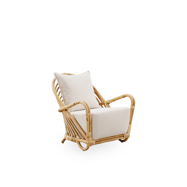 Vista lateral de la silla lounge Charlottenborg en ratán natural pulido, diseñada por Arne Jacobsen. La silla cuenta con respaldo curvado y reposabrazos integrados en la base, hecha a mano con ratán indonesio de alta calidad.