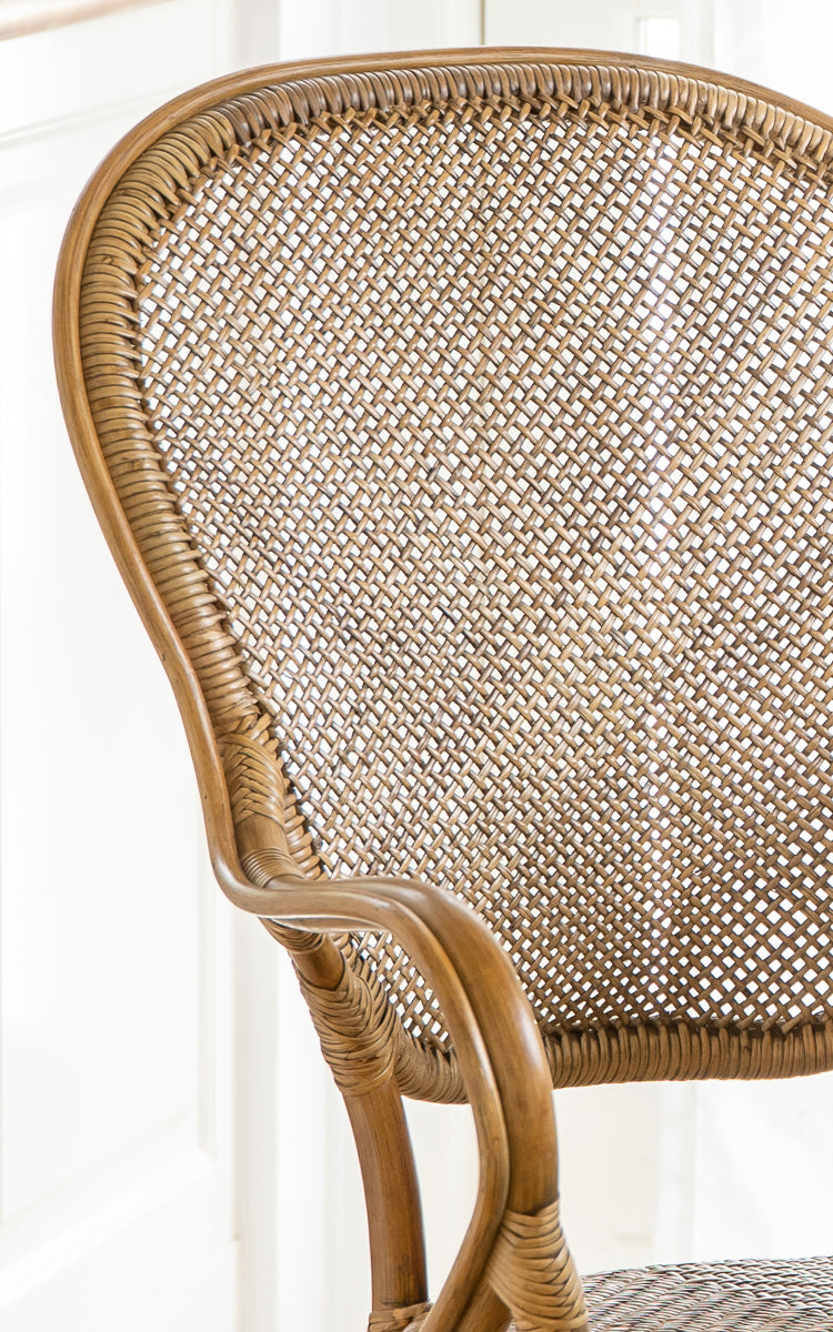Esta es una imagen de detalle de Rossini sillón de comedor en antique rattan. Detalle del reposabrazos curvo de ratán, asiento tejido y uniones envueltas.