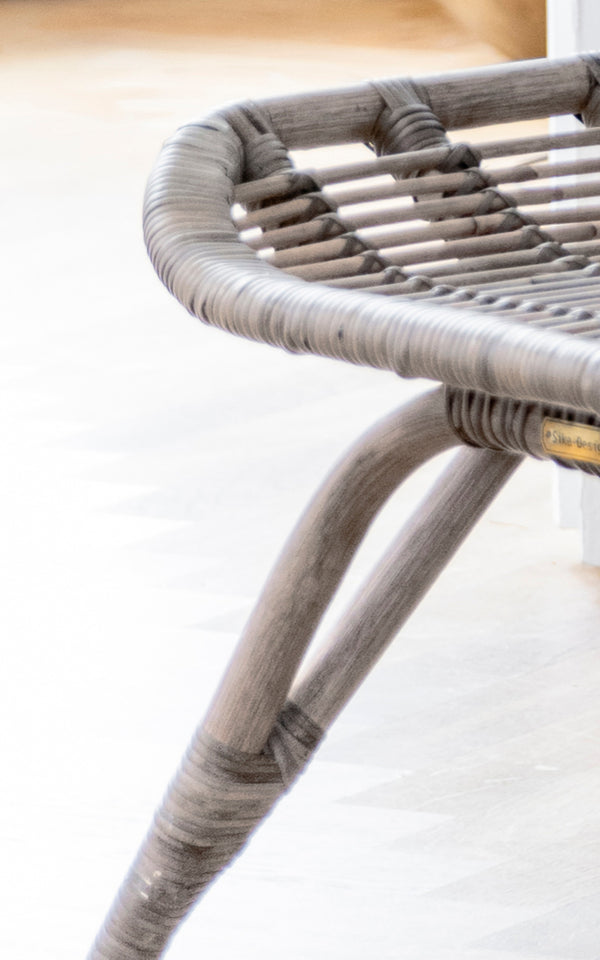 Esta es una imagen de detalle de Monet Footstool i taupe rattan. Detalle de la parte superior tejida del asiento y la estructura curvada en acabado taupe suave.