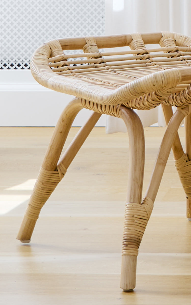 Esta es una imagen de detalle de Monet Footstool i natural rattan. Detalle del asiento tejido plano y las uniones de ratán envueltas en las patas.