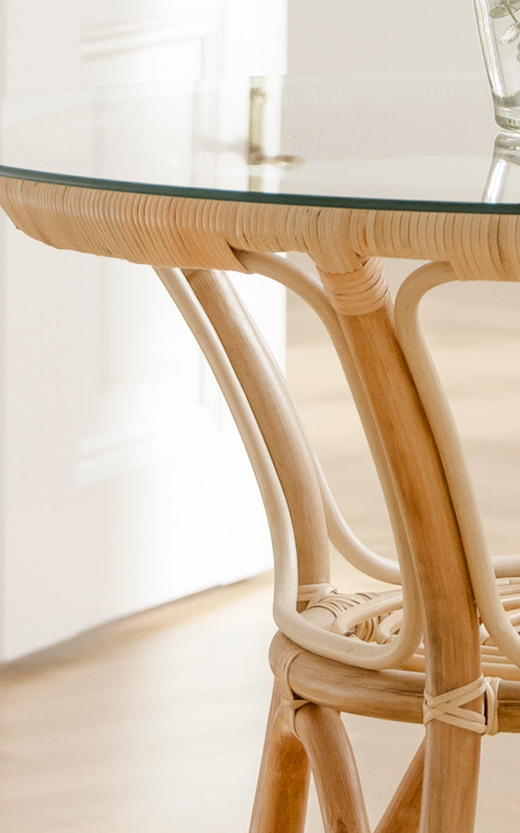 Esta es una imagen de detalle de Tony Café Table en natural rattan. Detalle del tablero redondo de vidrio con borde tejido de ratán y patas curvas.
