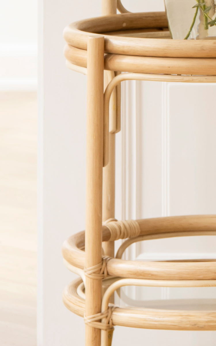 Esta es una imagen de detalle de Romeo Trolley i natural rattan. Detalle de la estructura de ratán de dos niveles con estante de cristal y ruedas de latón.
