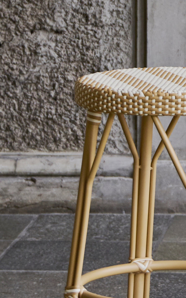 Esta es una imagen de detalle de Simone taburete en striped honey ivory ArtFibre Skin on Rattan frame. Junto a un muro de piedra.