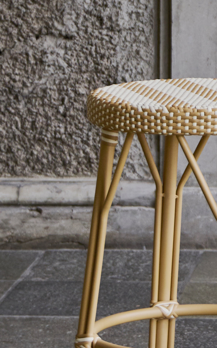 Esta es una imagen de detalle de Simone taburete en striped honey ivory ArtFibre Skin on Rattan frame. Junto a un muro de piedra.