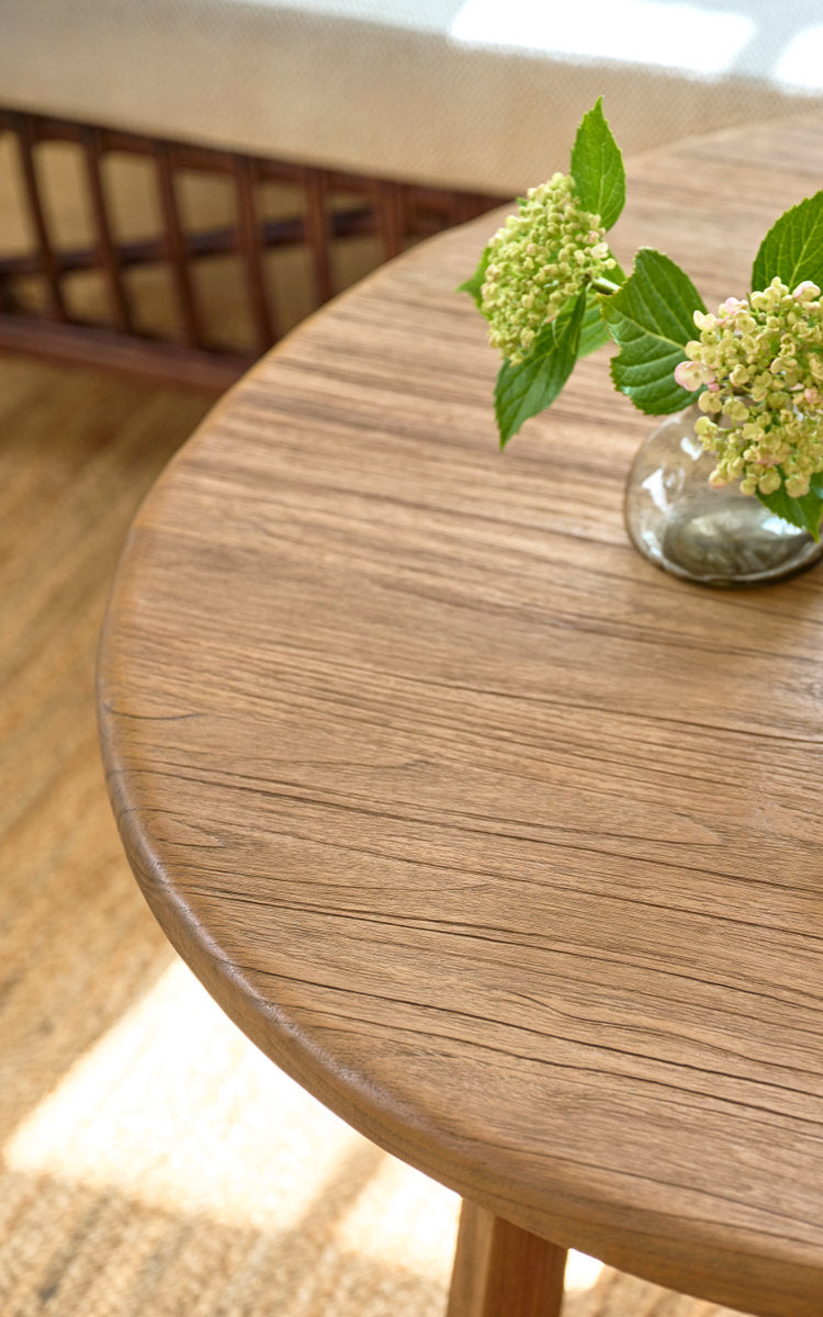 Esta es una imagen de detalle de Aksel mesa de centro Ø100 cm en teak indoor. Tapa redonda de teca con jarrón de hortensias sobre alfombra de yute.