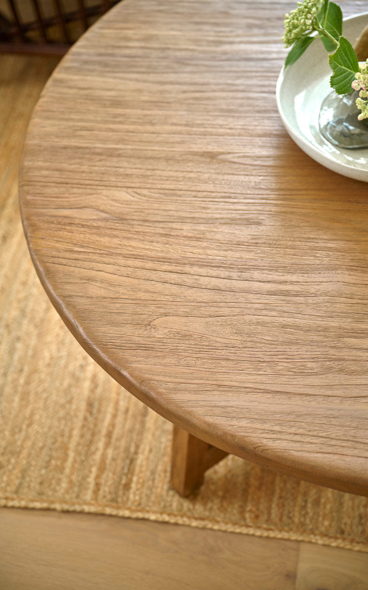 Esta es una imagen de detalle de Aksel mesa de centro Ø120 cm en teak indoor. Tapa redonda de teca con flores en un cuenco sobre alfombra de yute.