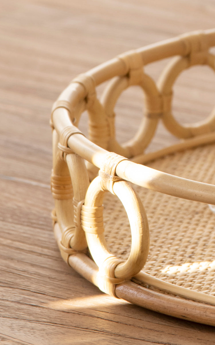 Esta es una imagen de detalle de Mira Tray i natural rattan. Detalle del borde circular de anillos y la base tejida de caña de la bandeja redonda.