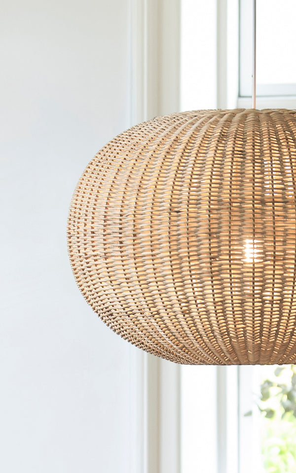 Esta es una imagen de detalle de Tangelo Lampshade Ø62 cm | Large en natural rattan. Detalle del tejido grande de ratán de la lámpara colgante redondeada junto a una ventana.