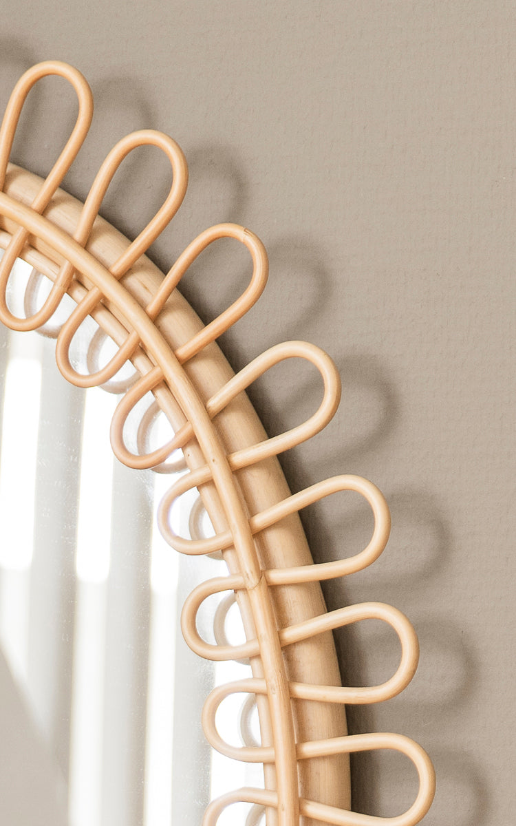 Esta es una imagen de detalle de Luella espejo en polished natural rattan. El marco decorativo de ratán en bucles proyecta elegantes sombras en la pared.