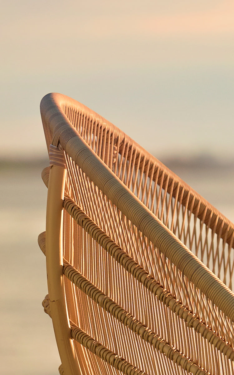 Esta es una imagen de detalle de Luna sillón lounge exterior en natural aluminium artfibre. El respaldo tejido brilla con la luz dorada del atardecer junto al mar.