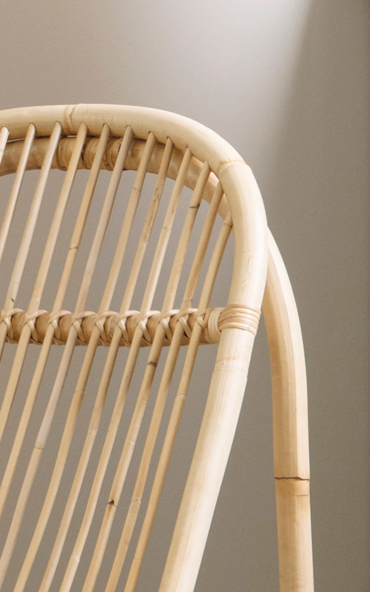 Esta es una imagen de detalle de Nanny Rocking Chair i polished natural rattan. Detalle de las varillas curvadas lisas y la base circular de balancín.