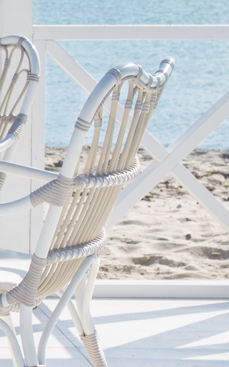 Esta es una imagen de detalle de Margret sillón de comedor exterior en dove white aluminium artfibre. Varillas blancas curvadas con juntas envueltas junto al mar.
