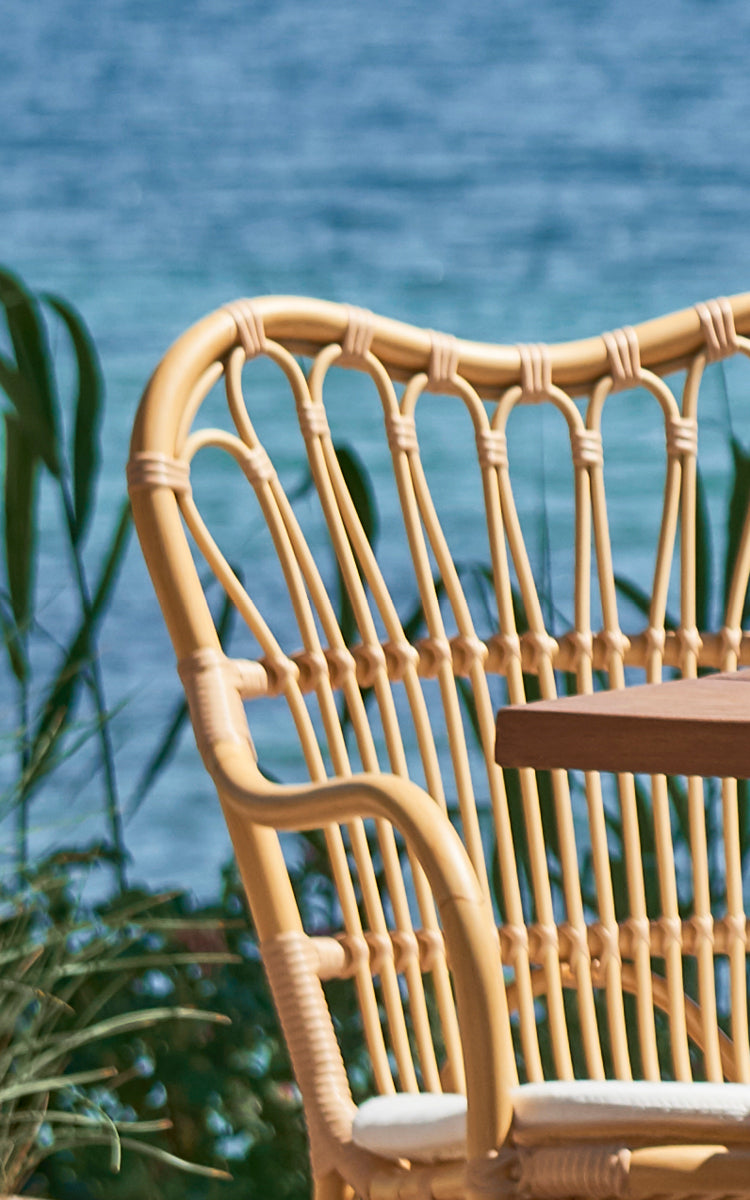Esta es una imagen de detalle de Margret sillón de comedor exterior en natural aluminium artfibre. Varillas curvadas del respaldo con vista al mar detrás.