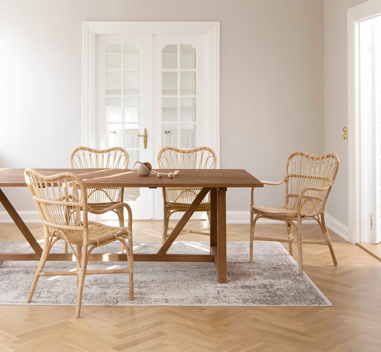 Esta es una imagen de estilo de vida de Margret silla de comedor en natural rattan. Colocada alrededor de una mesa de comedor de teca en una luminosa sala escandinava con suelo de roble.