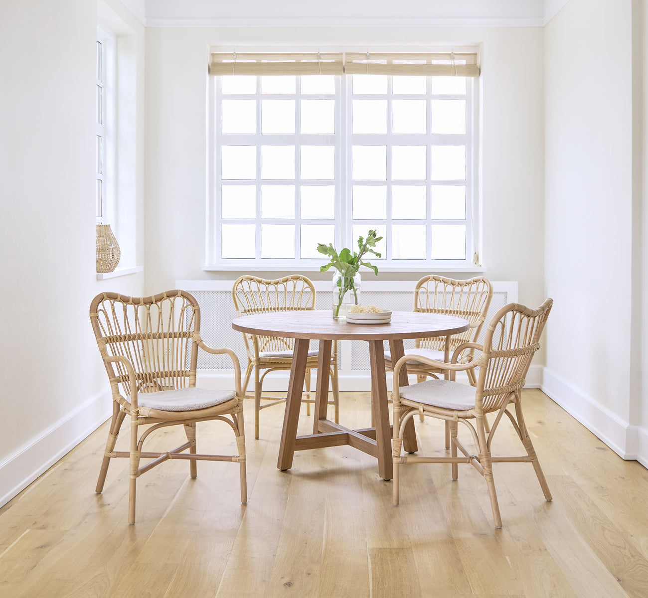 Esta es una imagen de estilo de vida de Margret silla de comedor en natural rattan. Luminosa sala blanca con mesa redonda de comedor y suelo de roble.
