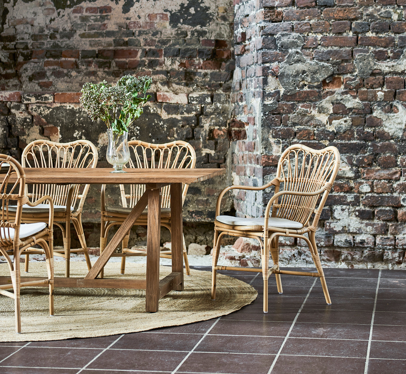 Esta es una imagen de estilo de vida de Margret silla de comedor en natural rattan. Loft industrial con pared de ladrillo visto y alfombra de yute.