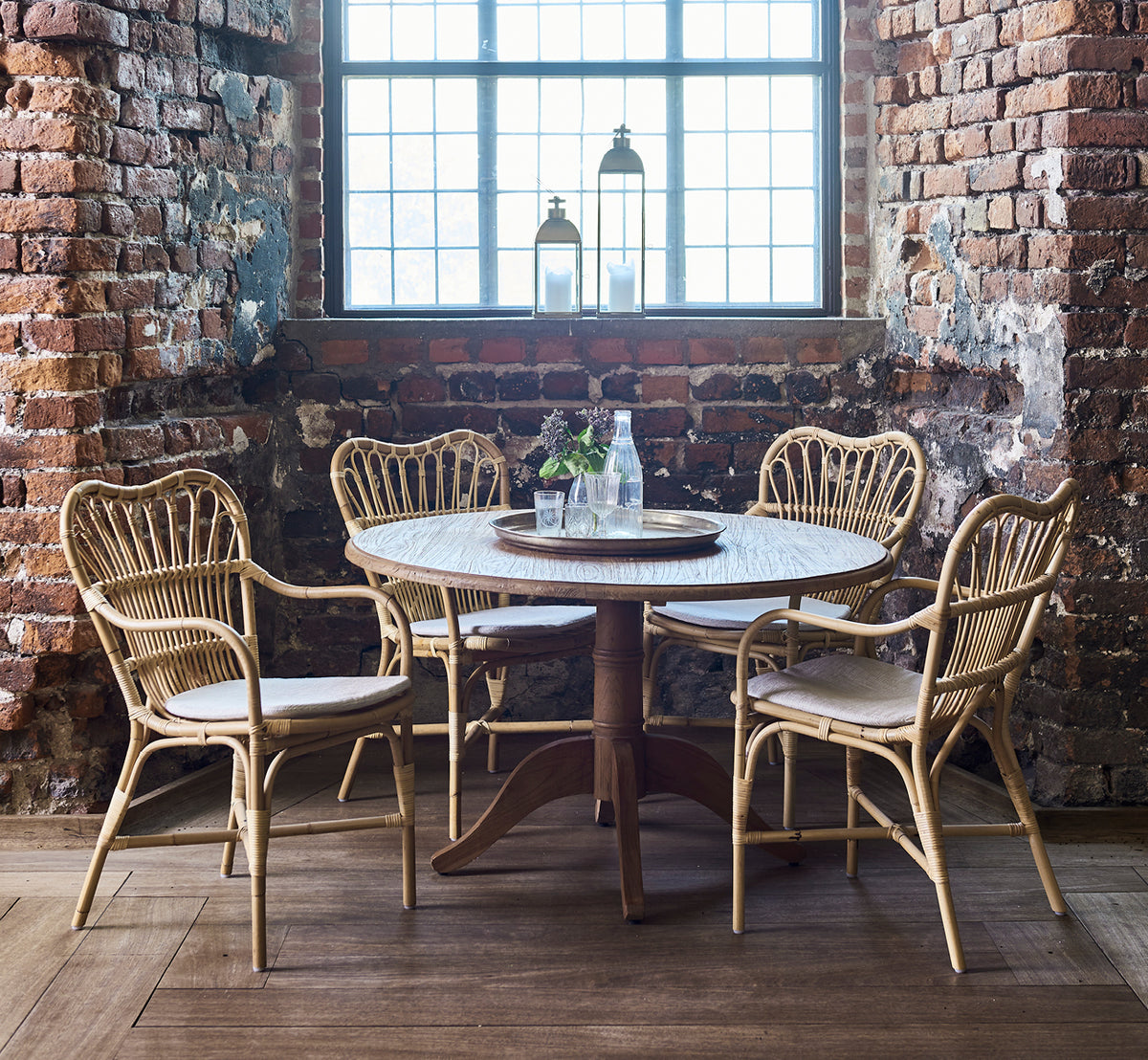 Esta es una imagen de estilo de vida de Margret silla de comedor en natural rattan. Interior rústico de ladrillo con mesa redonda y farol en el alféizar.