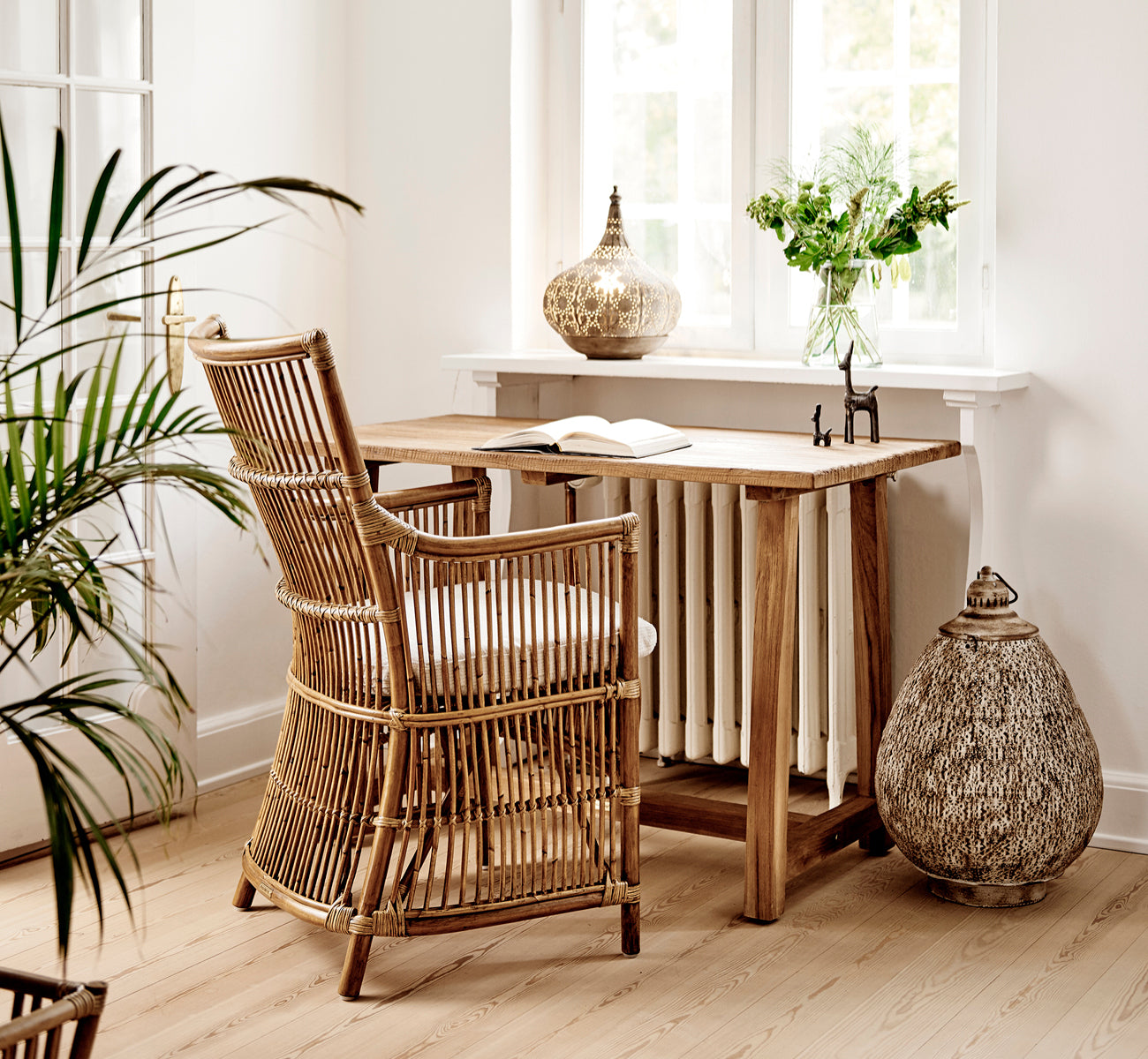 Esta es una imagen de estilo de vida de Davinci silla de comedor en antique rattan, en un interior luminoso con paredes de paneles blancos y parqué.