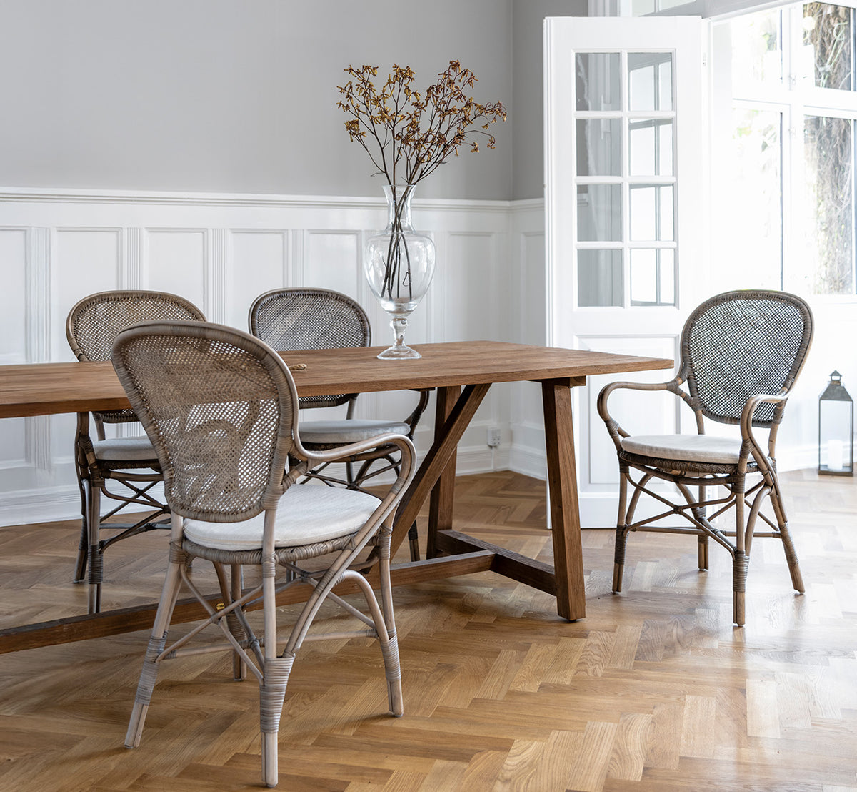 Esta es una imagen de estilo de vida de Rossini sillón de comedor en taupe rattan. Alrededor de una mesa de comedor de madera sobre un suelo de parqué en espiga.