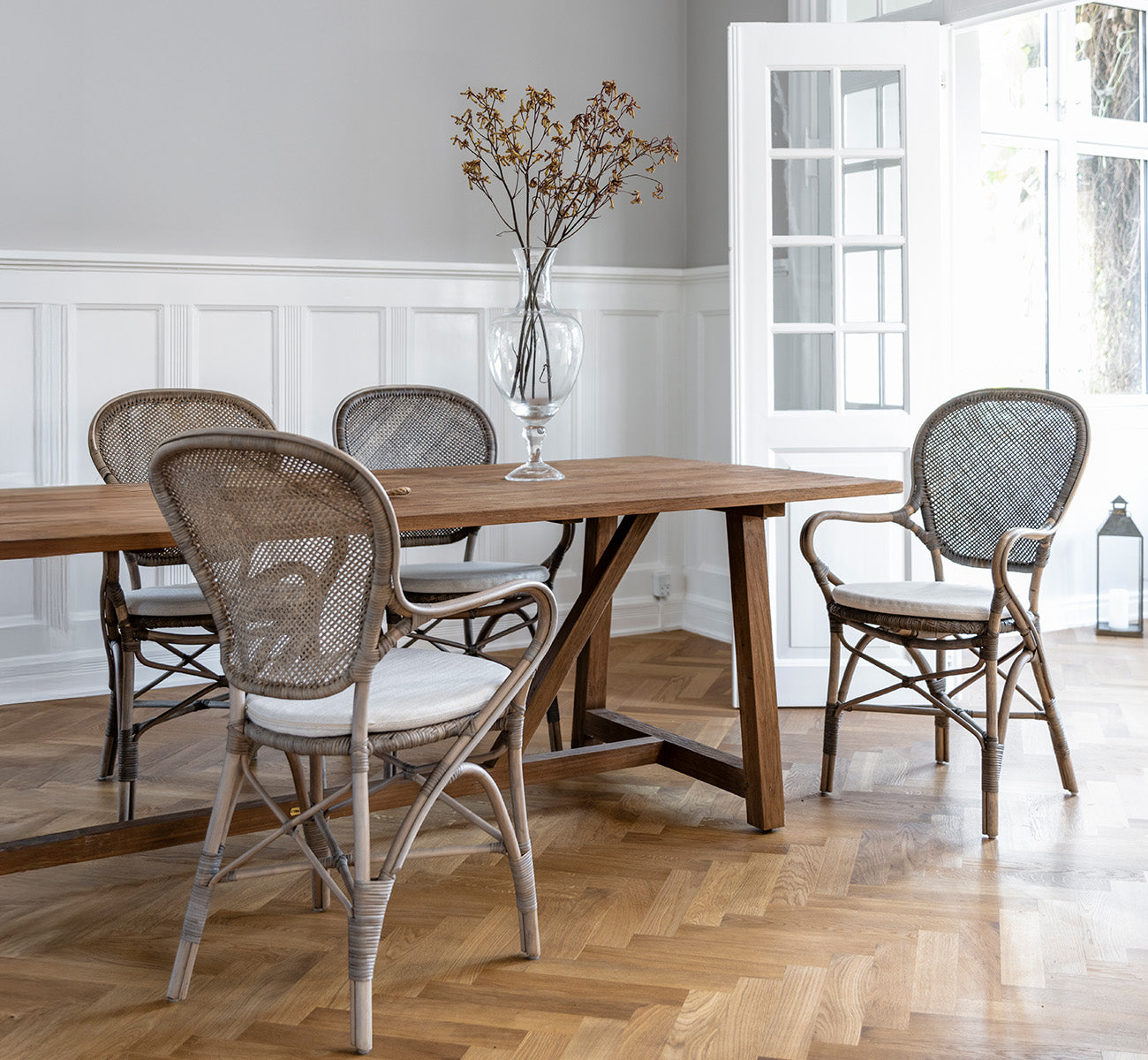 Esta es una imagen de estilo de vida de Rossini sillón de comedor en taupe rattan. Alrededor de una mesa de comedor de madera sobre un suelo de parqué en espiga.
