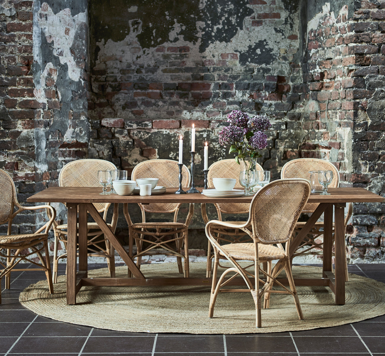 Esta es una imagen de estilo de vida de Rossini sillón de comedor en natural rattan. Combinada con una mesa redonda de vidrio sobre una alfombra de yute en una sala con paneles.