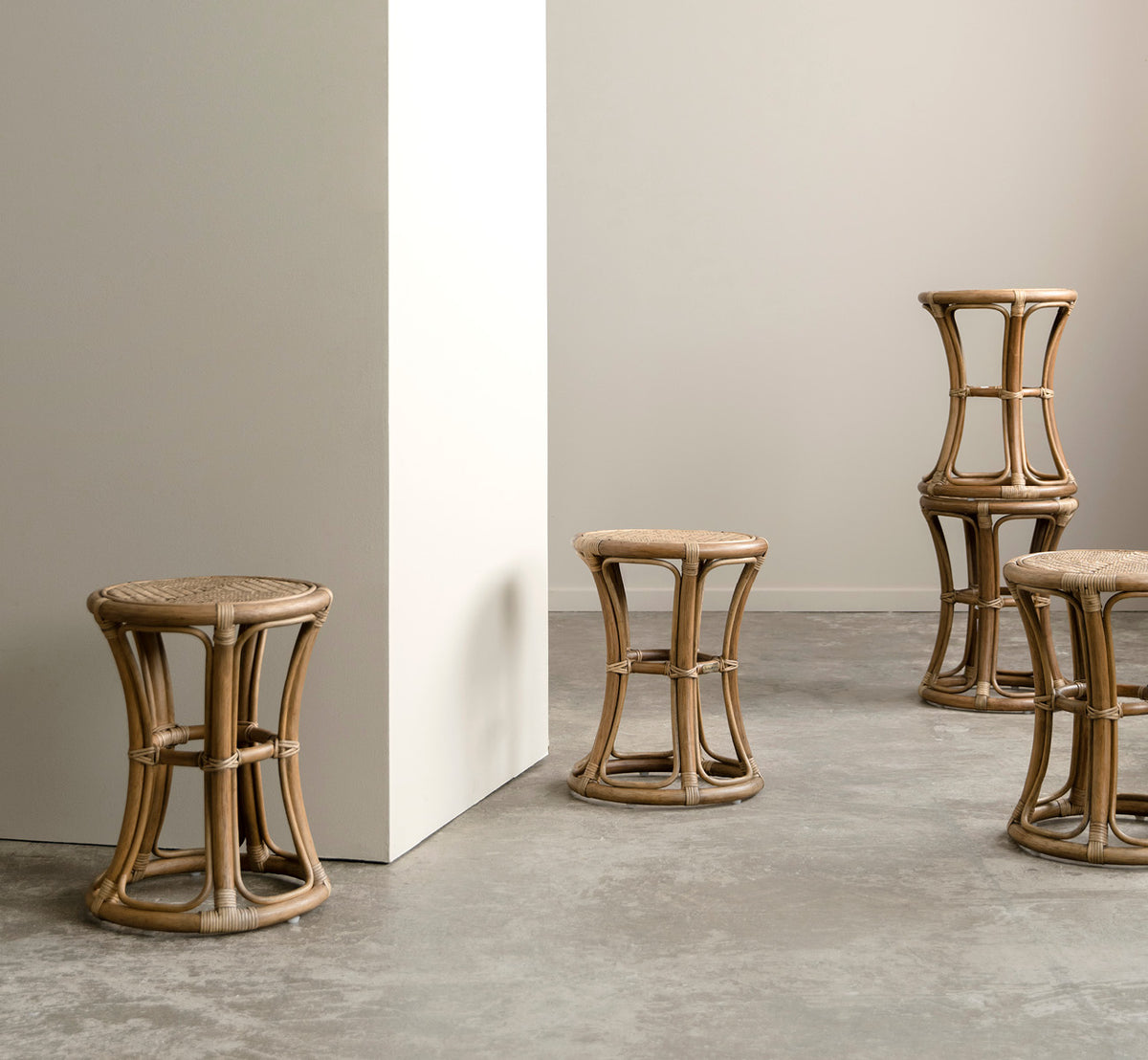 Esta es una imagen de estilo de vida de Bella taburete en antique rattan, en un interior luminoso con paredes de paneles blancos y parqué en espiga.