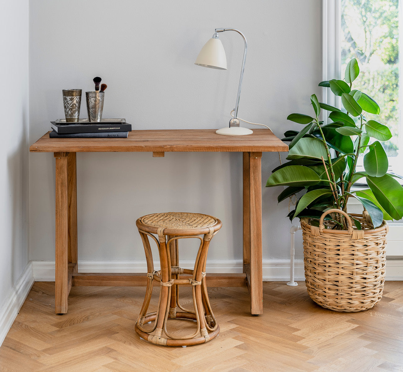 Esta es una imagen de estilo de vida de Bella taburete en antique rattan, en un interior luminoso con paredes de paneles blancos y parqué en espiga.