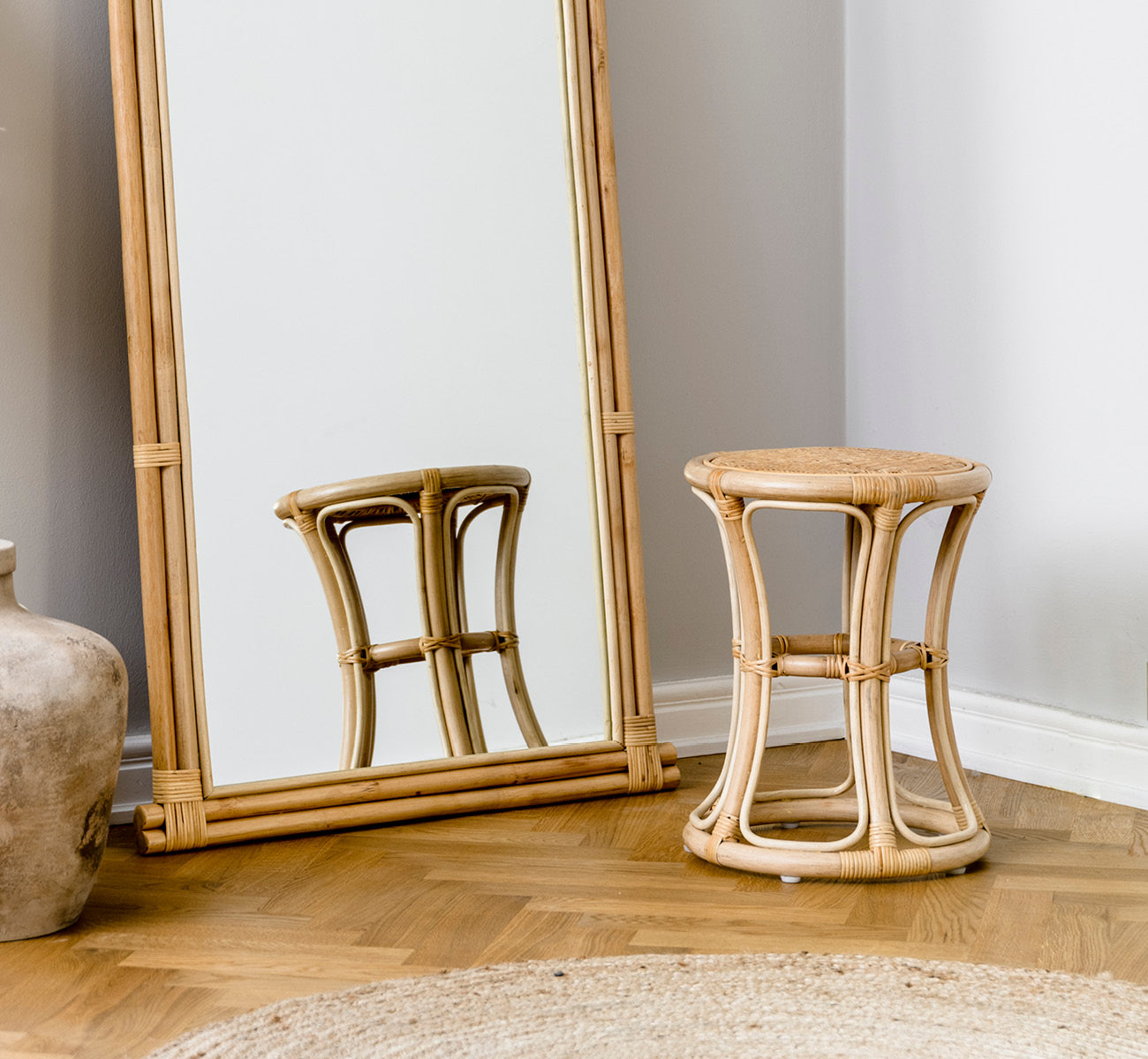 Esta es una imagen de estilo de vida de Bella taburete en natural rattan, en un interior luminoso con paredes de paneles blancos y parqué en espiga.