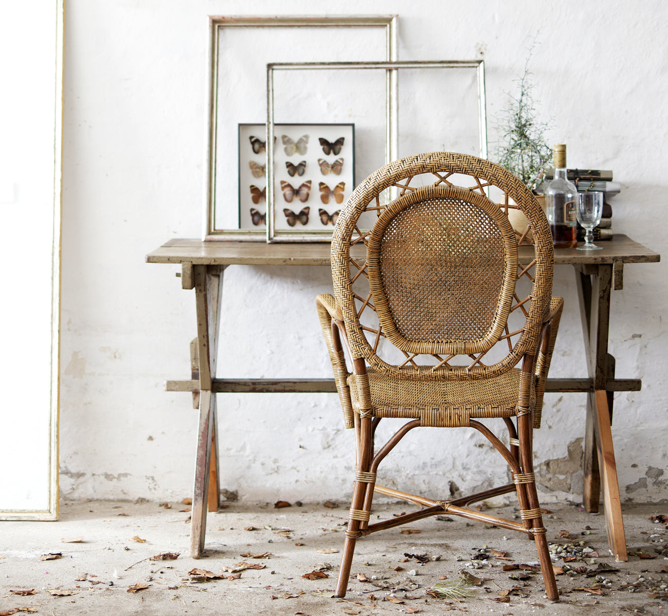 Esta es una imagen de estilo de vida de Romantica silla de comedor en antique rattan. Estilizada junto a una mesa de madera rústica con arte enmarcado en un ambiente vintage.