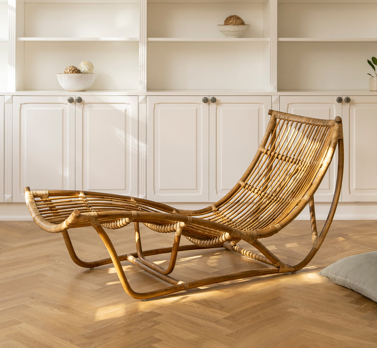 Esta es una imagen de estilo de vida de Michelangelo Daybed i antique rattan. Colocado en una sala blanca iluminada por el sol con suelo de parqué en espiga.