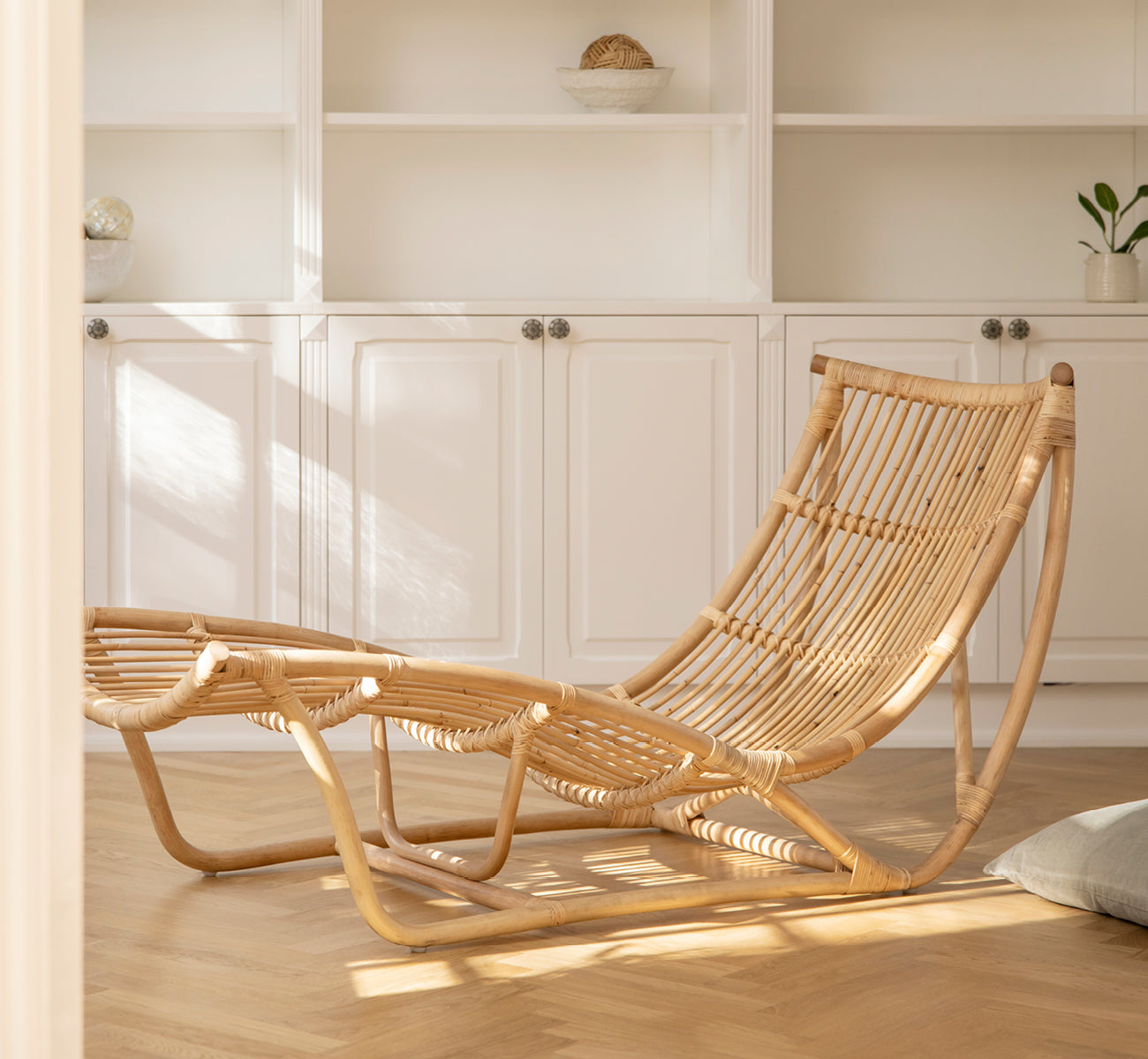 Esta es una imagen de estilo de vida de Michelangelo Daybed i natural rattan. Colocado en una sala blanca luminosa con suelo de hormigón y lámpara rosa.
