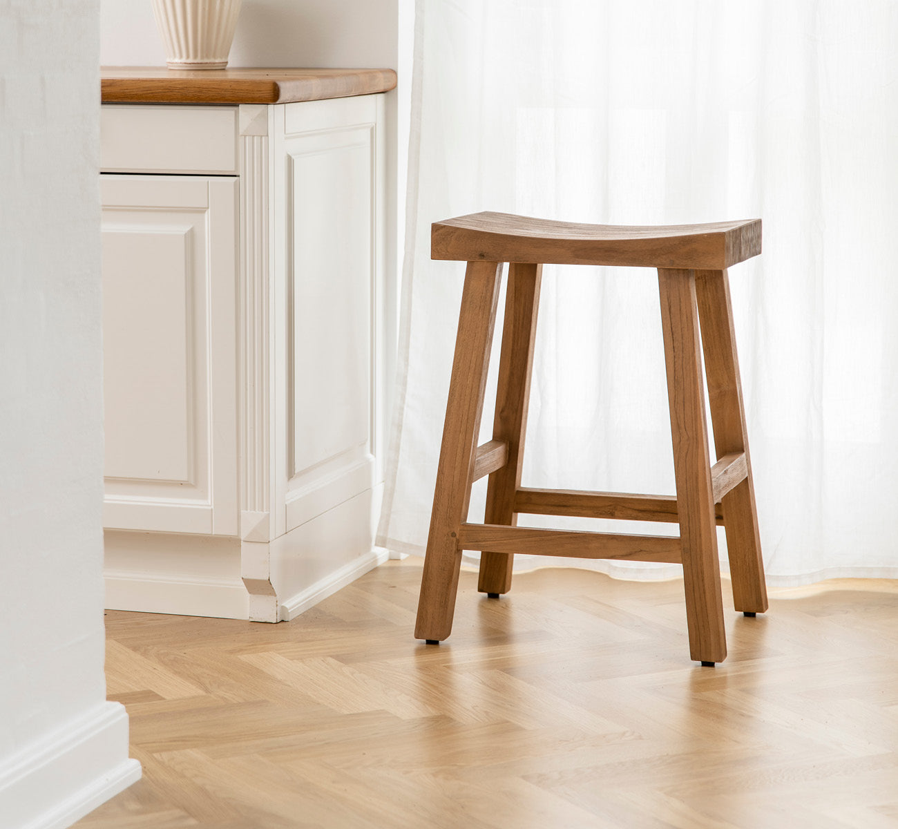 Esta es una imagen de estilo de vida de Charles taburete alto en teak indoor, en un interior blanco y luminoso con revestimiento de pared y parqué en.