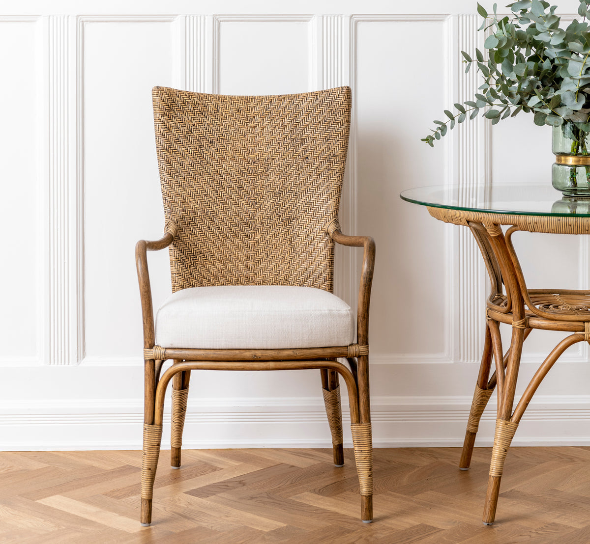 Esta es una imagen de estilo de vida de Melody Dining Armchair i antique rattan. Colocado junto a una mesa de comedor blanca en una luminosa sala escandinava.