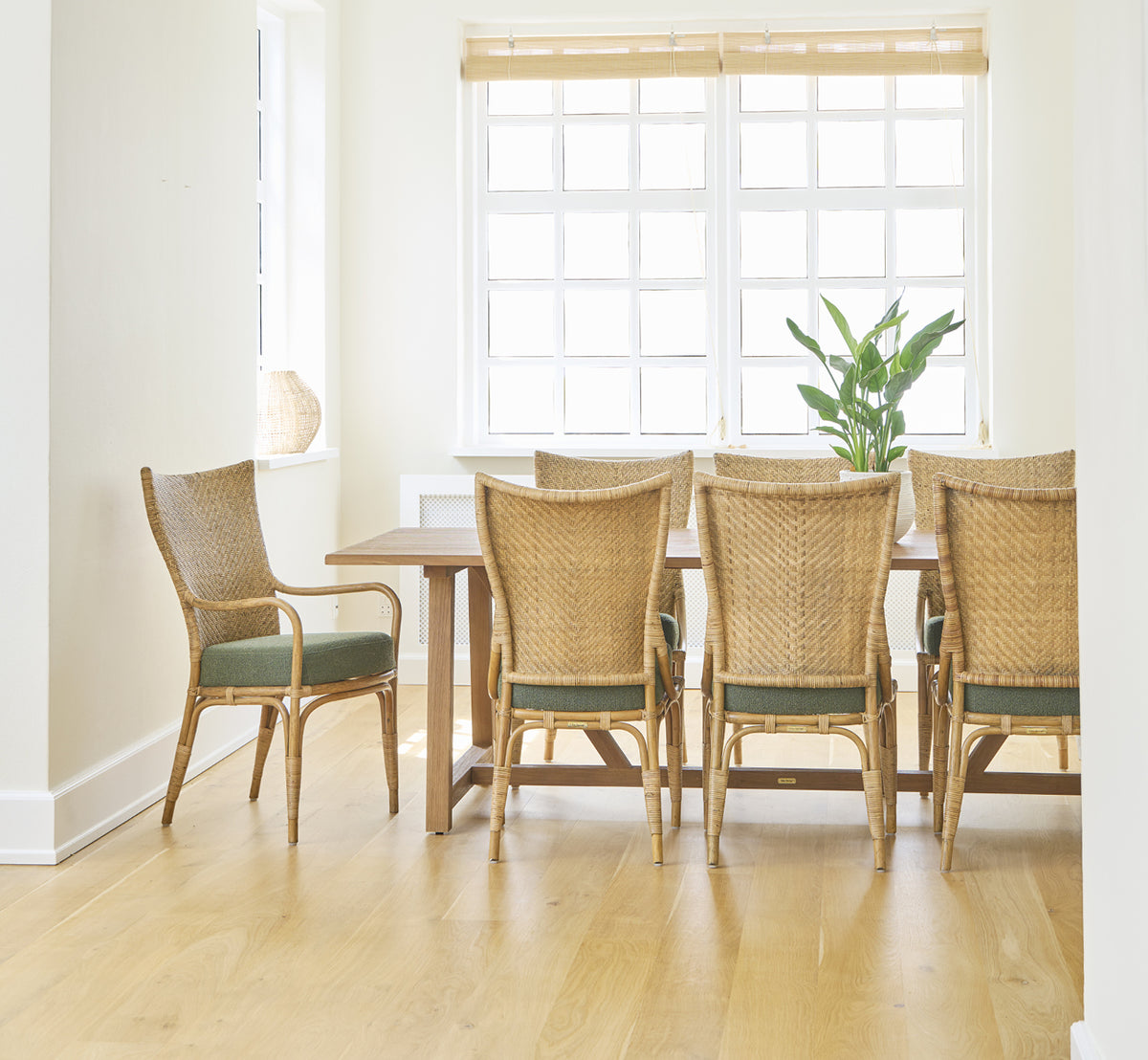 Esta es una imagen de estilo de vida de Melody Dining Armchair i antique rattan. Seis sillas junto a una mesa de teca en una sala luminosa con suelo de roble.