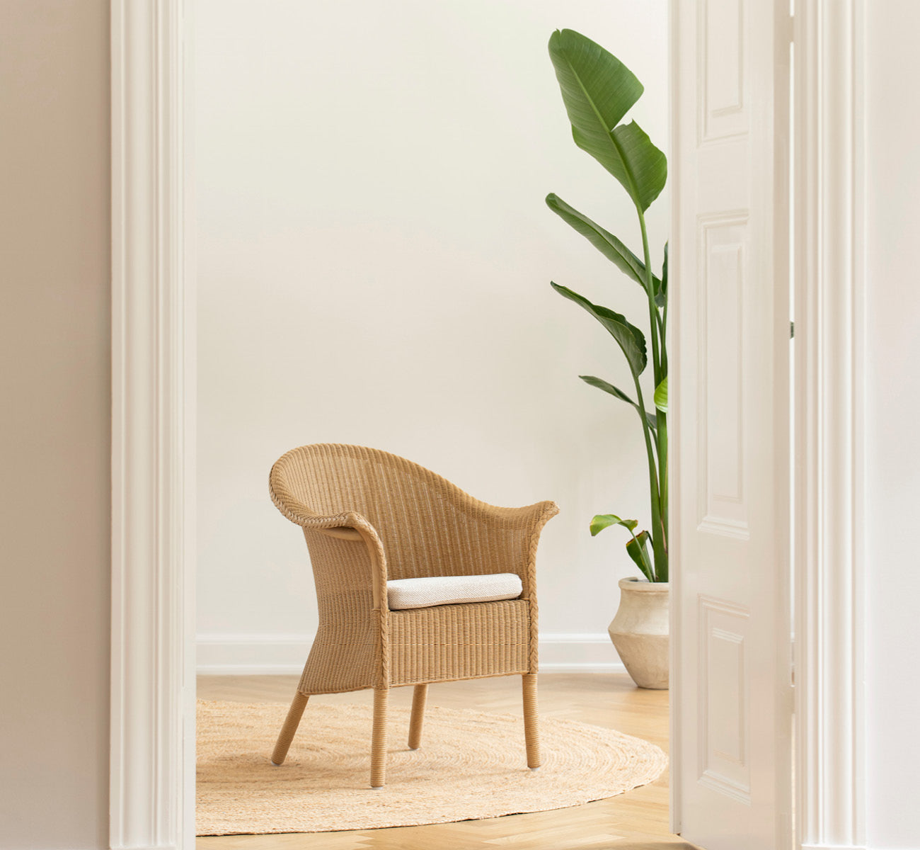 Esta es una imagen de estilo de vida de Classic silla de comedor en natural Loom Rattan Frame, en un interior luminoso con paredes de paneles blancos.