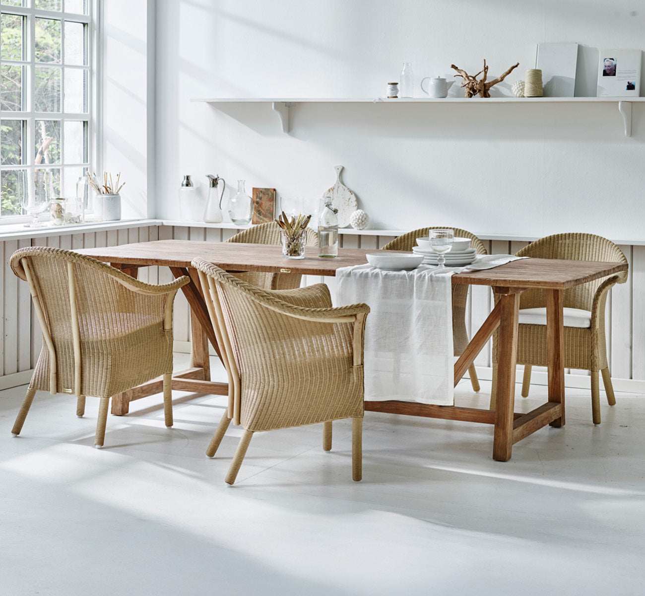 Esta es una imagen de estilo de vida de Classic silla de comedor en natural Loom Rattan Frame, en un interior luminoso con paredes de paneles blancos.