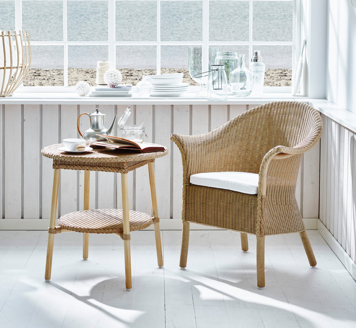 Esta es una imagen de estilo de vida de Classic silla de comedor en natural Loom Rattan Frame, en un interior luminoso con paredes de paneles blancos.
