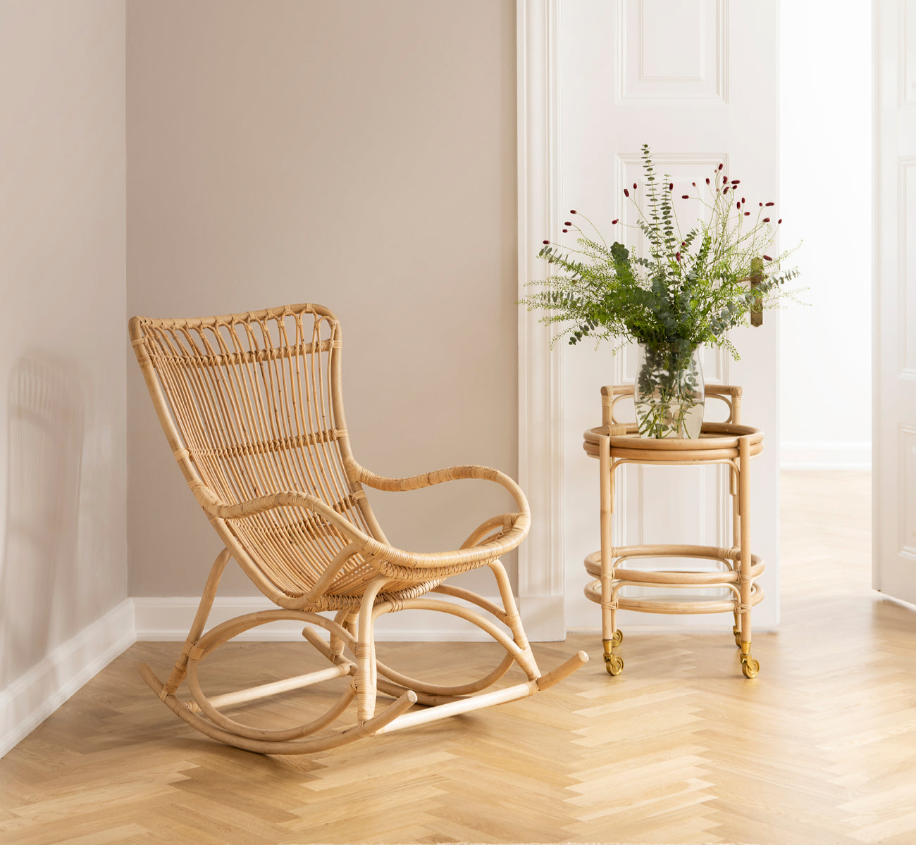 Esta es una imagen de estilo de vida de Monet Rocking Chair i natural rattan. En un rincón acogedor con suelo en espiga y carrito de ratán.